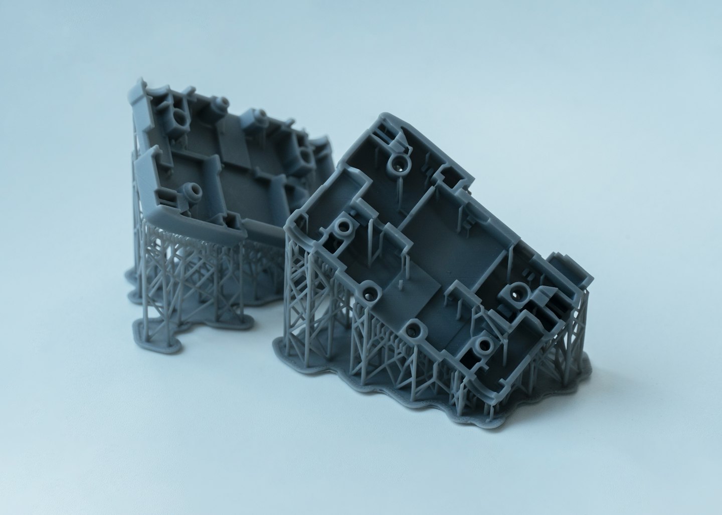 Zwei graue 3D-gedruckte Harzprototypen mit angebrachten Stützstrukturen.